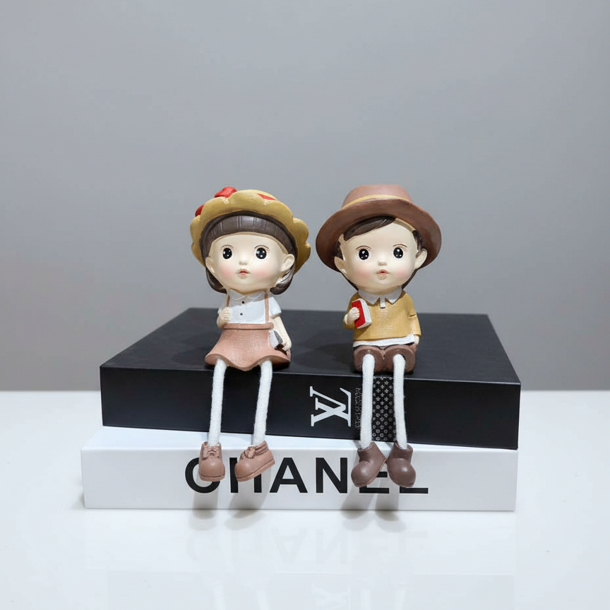 Two ceramic figurines on a Chanel box with a gray background
