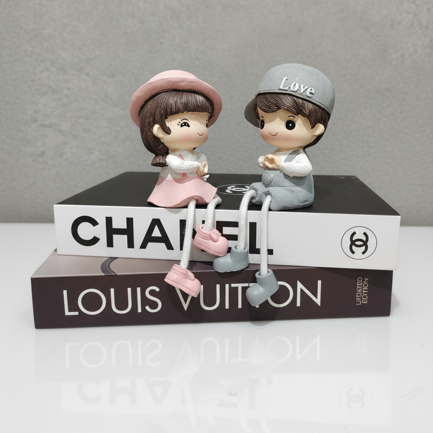 Two small figurines sitting on top of Chanel and Louis Vuitton books with a gray background.