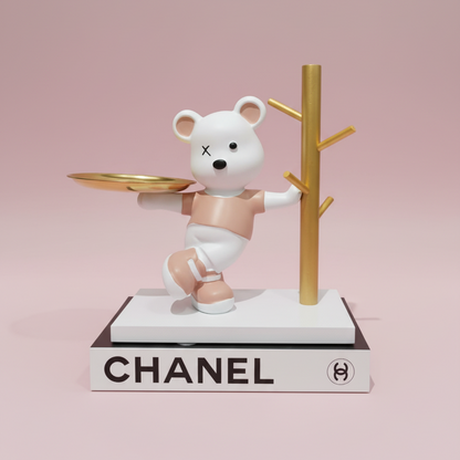 Bear figurine with a tray on a Chanel book against a pink background