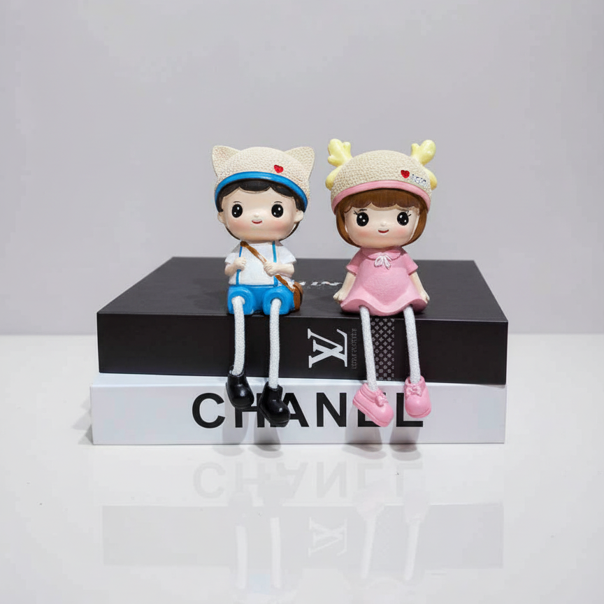 Two small figurines sitting on a Chanel box with a plain background