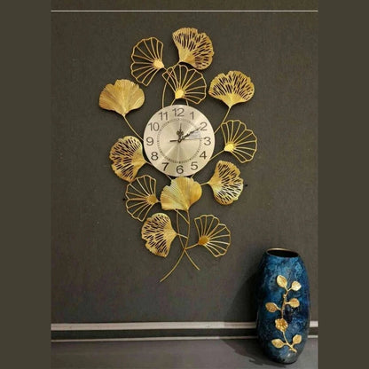 Decorative wall clock with gold leaf design on a dark wall, next to a blue vase.
